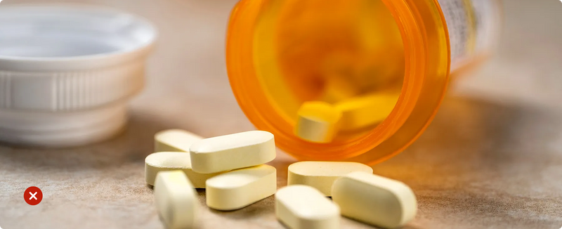 Yellow pills spilling out of an orange prescription bottle on a wooden surface.