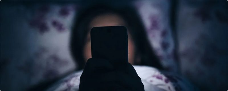 Person holding a smartphone in a dimly lit room with floral curtains.