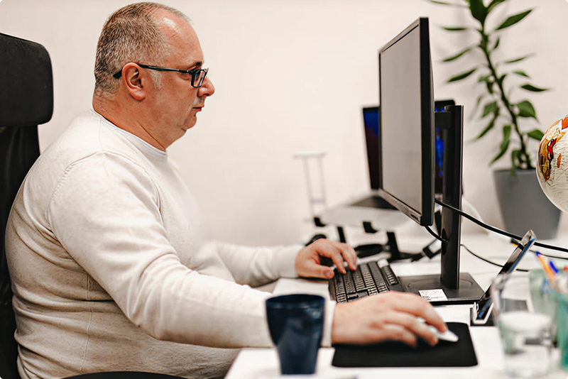 Man working at a desk with multiple computer monitors and office supplies.